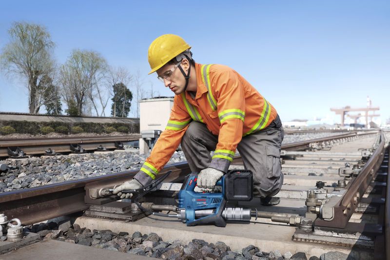 บุคคลที่สวมอุปกรณ์ด้านความปลอดภัยใช้ปืนจารบีไร้สายเพื่อบำรุงรักษารางรถไฟ.