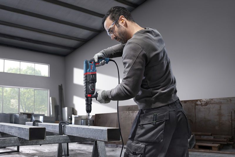 บุคคลที่สวมอุปกรณ์ด้านความปลอดภัยกำลังเจาะเข้าไปในคานเหล็กโดยใช้ค้อนโรตารี่.