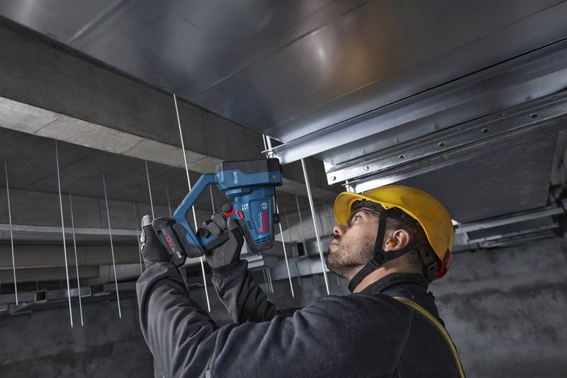 บุคคลที่สวมอุปกรณ์ด้านความปลอดภัยใช้เครื่องตัดเกลียวแบบไร้สายตัดแท่งเพดาน.