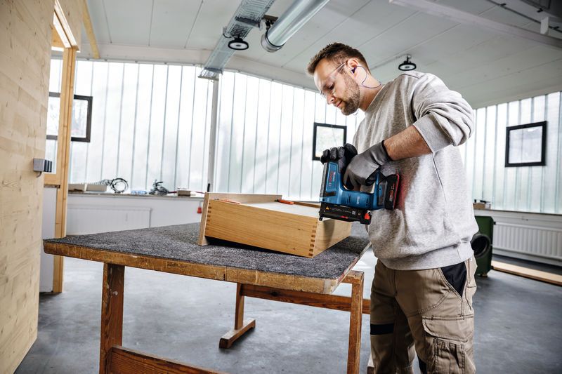 บุคคลที่สวมอุปกรณ์ด้านความปลอดภัยใช้ปืนยิงตะปูไร้สายบนกล่องไม้ในโรงงาน.