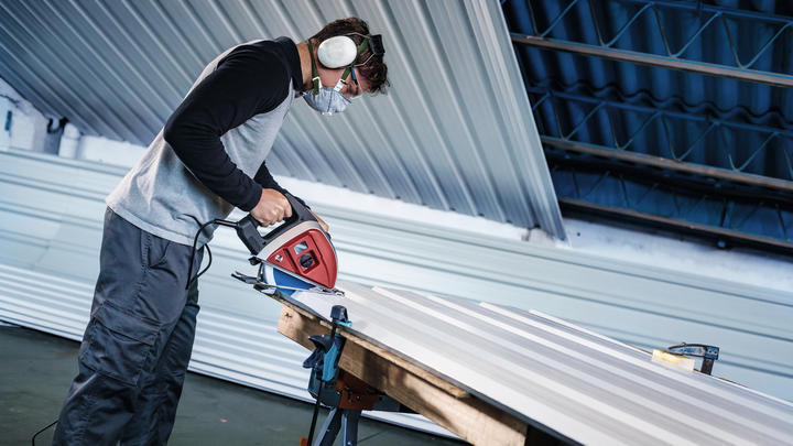 ผู้ที่สวมอุปกรณ์ความปลอดภัยกำลังตัดแผ่นโลหะด้วยเลื่อยไฟฟ้า