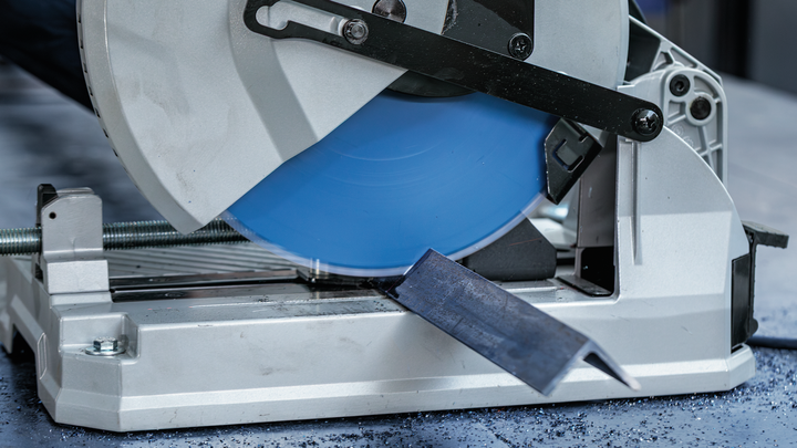 ใบเลื่อยตัดโลหะตัดผ่านแท่งเหล็กบนพื้นโรงงาน.