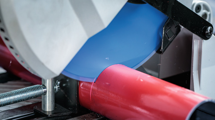 ใบเลื่อยตัดโลหะจะตัดผ่านท่อสีแดงที่ยึดไว้ในที่หนีบ.