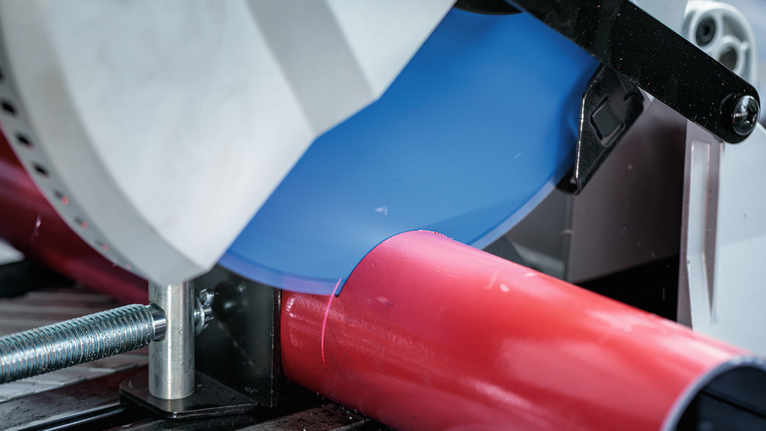 ใบเลื่อยตัดโลหะจะตัดผ่านท่อสีแดงที่ยึดไว้ในที่หนีบ.