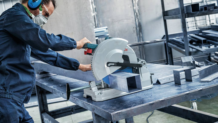 บุคคลที่สวมอุปกรณ์ป้องกันความปลอดภัยกำลังตัดคานโลหะด้วยเลื่อยวงเดือนในโรงงาน.