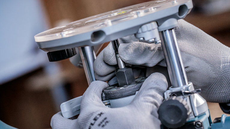 บุคคลที่สวมอุปกรณ์ด้านความปลอดภัยกำลังปรับเครื่องมือเราเตอร์โดยใช้มือที่สวมถุงมือ.