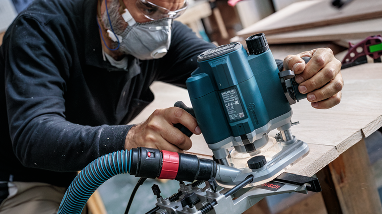 บุคคลที่สวมอุปกรณ์ความปลอดภัยใช้เราเตอร์ไฟฟ้าเพื่อขึ้นรูปขอบแผ่นไม้.