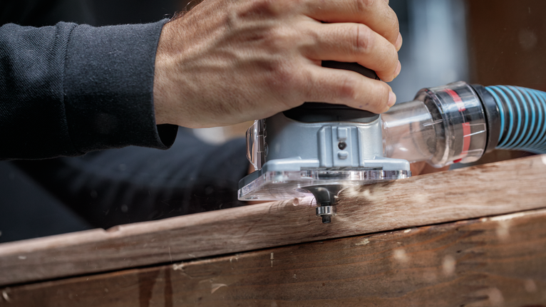 ผู้ใช้งานกำลังนำเราเตอร์ไฟฟ้าไปตามแผ่นไม้เพื่อกำหนดขอบให้แม่นยำ.