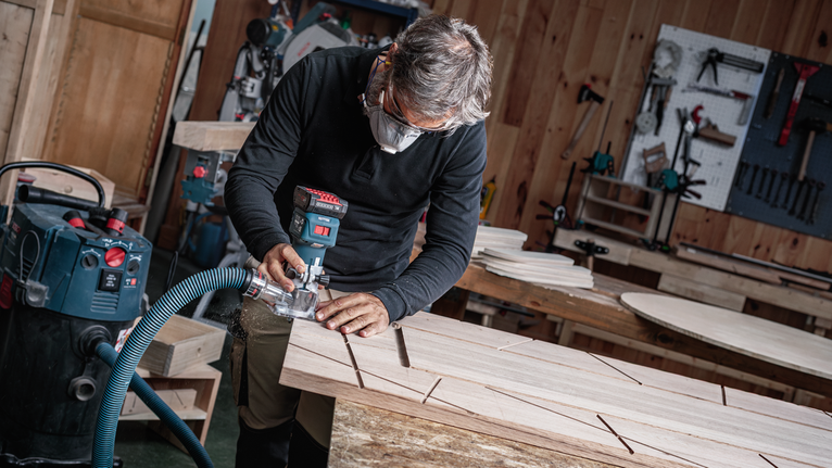 บุคคลที่สวมอุปกรณ์ด้านความปลอดภัยใช้เครื่องมือไฟฟ้าในการกัดร่องบนแผ่นไม้.