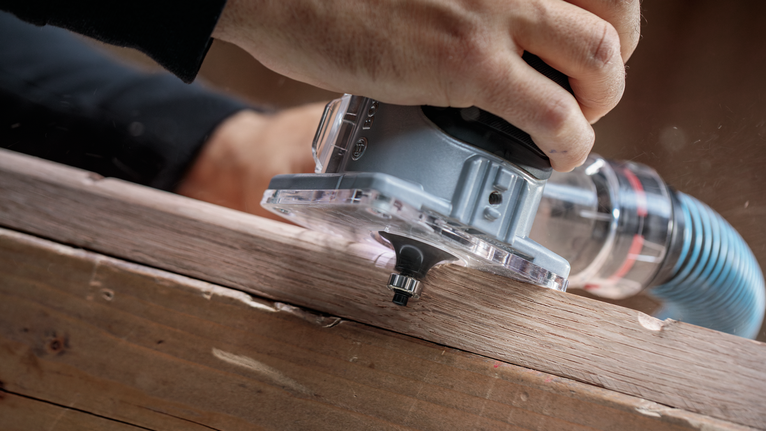 ผู้ใช้ใช้เราเตอร์แบบพกพาเพื่อขึ้นรูปขอบแผ่นไม้.