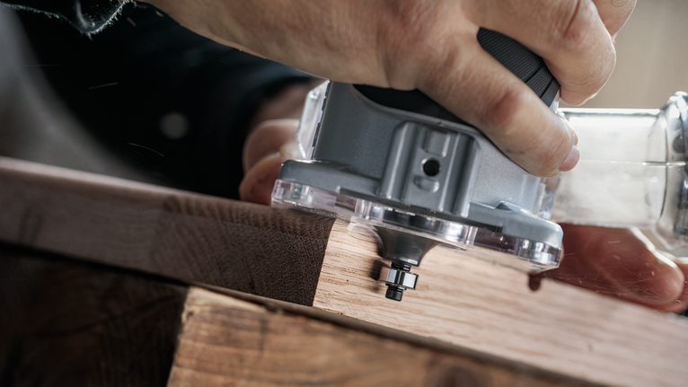 คนกำลังควบคุมเครื่องตัดหญ้าไฟฟ้าไปตามขอบแผ่นไม้.