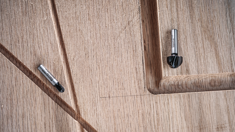 ดอกเราเตอร์ 2 ดอกวางอยู่บนพื้นผิวไม้แกะสลักที่มีรายละเอียดเป็นร่อง.