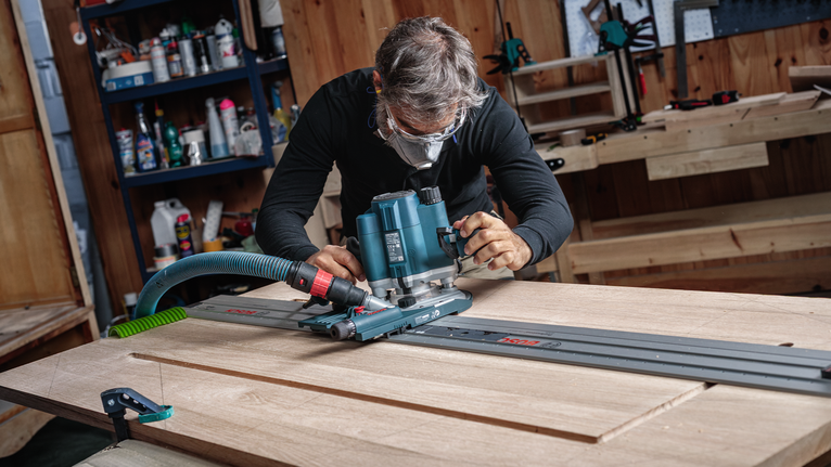 บุคคลที่สวมอุปกรณ์ความปลอดภัยกำลังนำเราเตอร์ไปตามรางเพื่อสร้างแผ่นไม้.