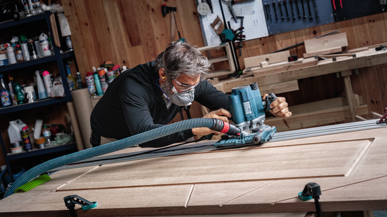 บุคคลที่สวมอุปกรณ์ด้านความปลอดภัยใช้เครื่องมือไฟฟ้าในการกัดร่องในประตูไม้.