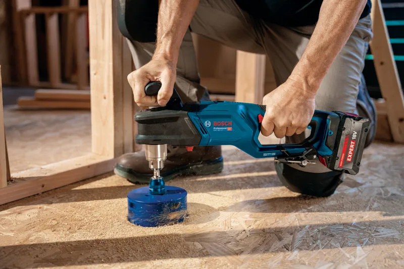 คนใช้สว่านไร้สายเจาะรูขนาดใหญ่ในพื้นไม้.