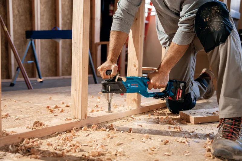 บุคคลที่สวมอุปกรณ์ความปลอดภัยกำลังเจาะโครงไม้ด้วยสว่านกระแทกไร้สาย.