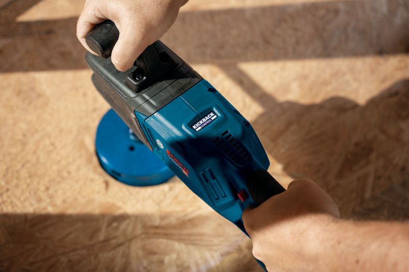 บุคคลหนึ่งกำลังใช้งานสว่านไร้สายสีน้ำเงินบนพื้นไม้.