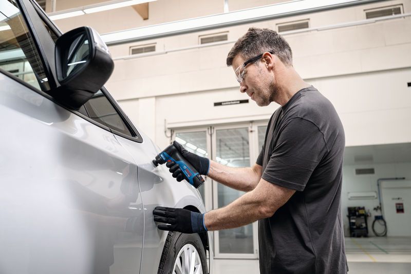 บุคคลที่สวมอุปกรณ์ด้านความปลอดภัยกำลังขัดประตูรถโดยใช้เครื่องขัดกระดาษทรายแบบสั่น