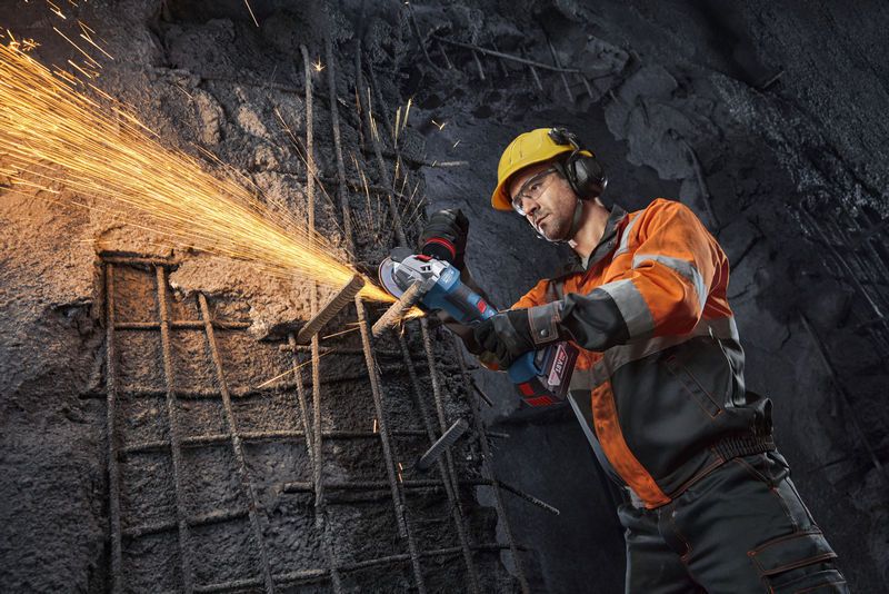 บุคคลที่สวมอุปกรณ์ความปลอดภัยกำลังใช้เครื่องเจียรไฟฟ้าตัดเหล็กเส้น ทำให้เกิดประกายไฟ