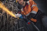 คนงานที่สวมอุปกรณ์ความปลอดภัยกำลังใช้เครื่องเจียรตัดเหล็กเส้นเสริมแรง