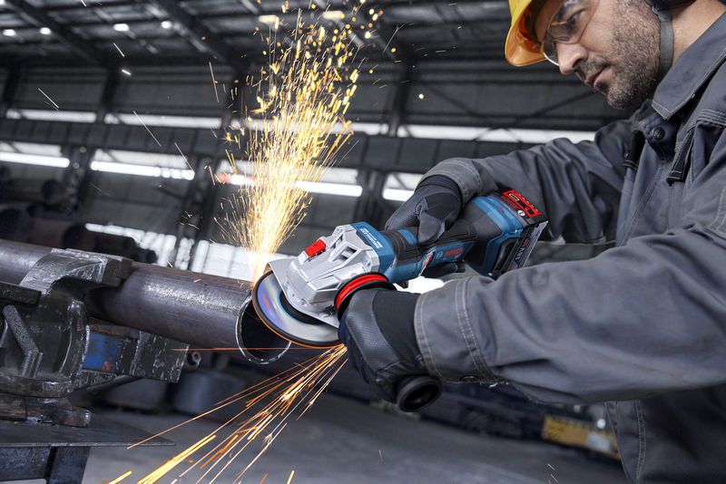 บุคคลที่สวมอุปกรณ์ป้องกันความปลอดภัยกำลังใช้เครื่องเจียรไฟฟ้าเจียรท่อโลหะ ทำให้เกิดประกายไฟ