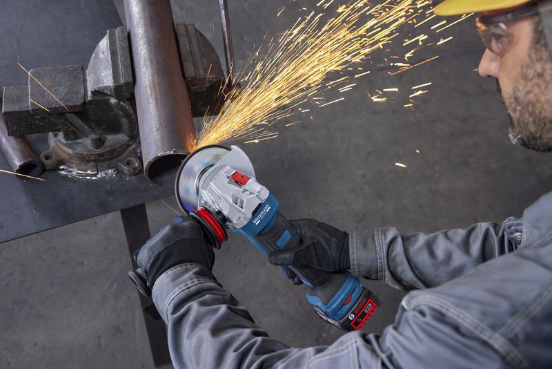 บุคคลที่สวมอุปกรณ์ความปลอดภัยกำลังใช้เครื่องเจียรตัดท่อโลหะ