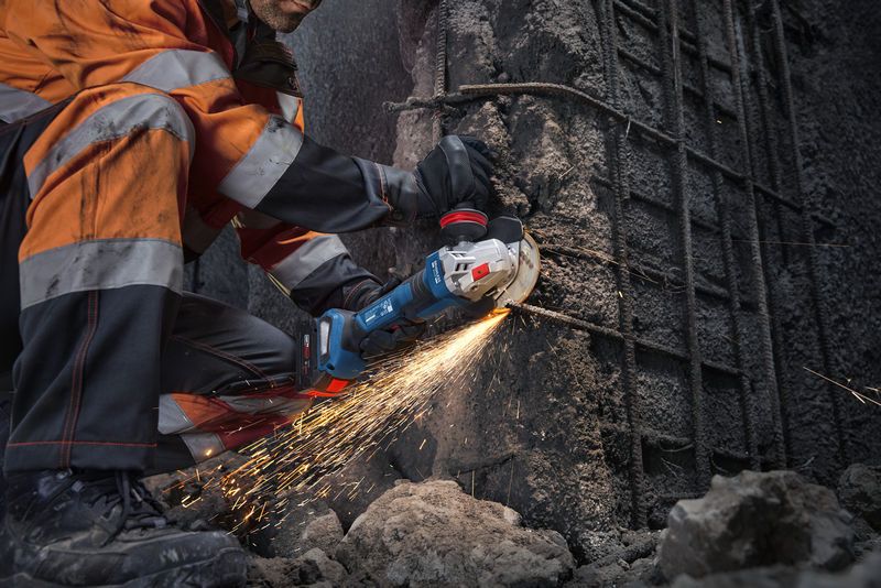 บุคคลที่สวมอุปกรณ์ความปลอดภัยกำลังตัดคอนกรีตด้วยเครื่องเจียรไฟฟ้า ทำให้เกิดประกายไฟ