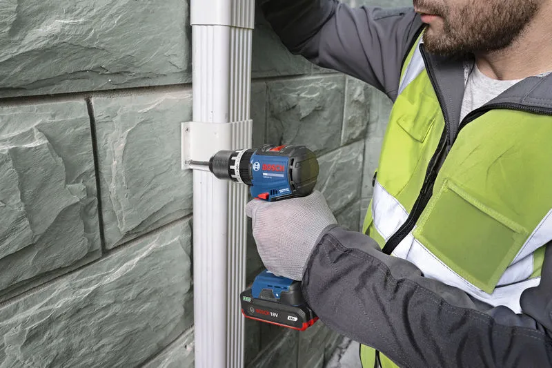 บุคคลที่สวมอุปกรณ์ป้องกันความปลอดภัยกำลังใช้สว่านไร้สายเพื่อยึดเหล็กยึดเข้ากับผนัง