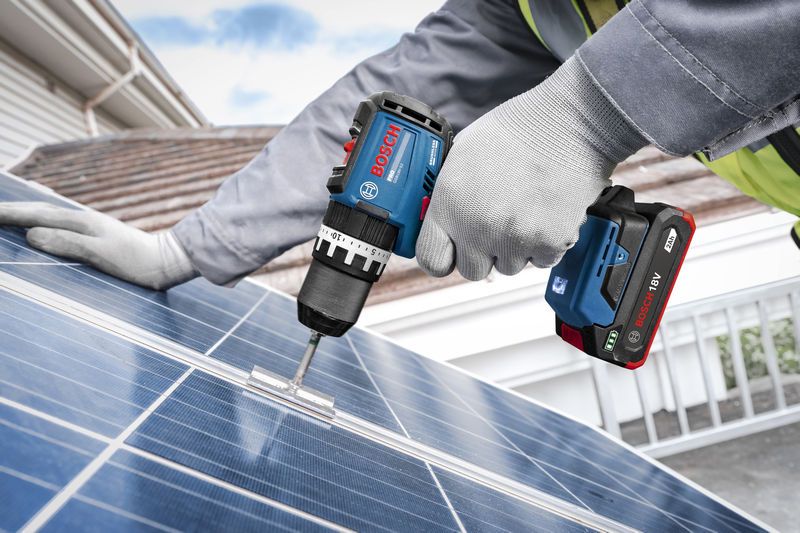 บุคคลที่สวมอุปกรณ์ความปลอดภัยกำลังยึดฐานยึดเข้ากับแผงโซลาร์เซลล์โดยใช้สว่านกระแทกไร้สาย