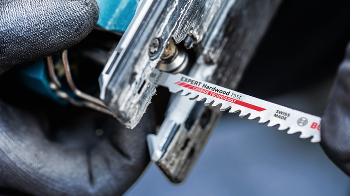 บุคคลที่สวมอุปกรณ์ด้านความปลอดภัยกำลังเสียบใบเลื่อยจิ๊กซอว์เข้าไปในเครื่องมือไฟฟ้า.