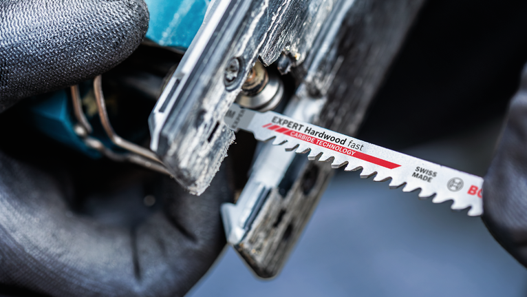 บุคคลที่สวมอุปกรณ์ด้านความปลอดภัยกำลังเสียบใบเลื่อยจิ๊กซอว์เข้าไปในเครื่องมือไฟฟ้า.