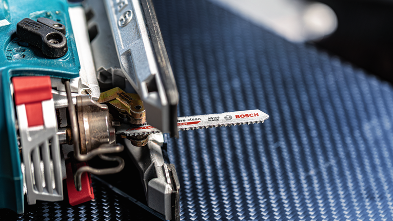 จิ๊กซอว์ที่มีใบเลื่อยโลหะวางอยู่บนพื้นผิวสีน้ำเงินที่มีลวดลาย.