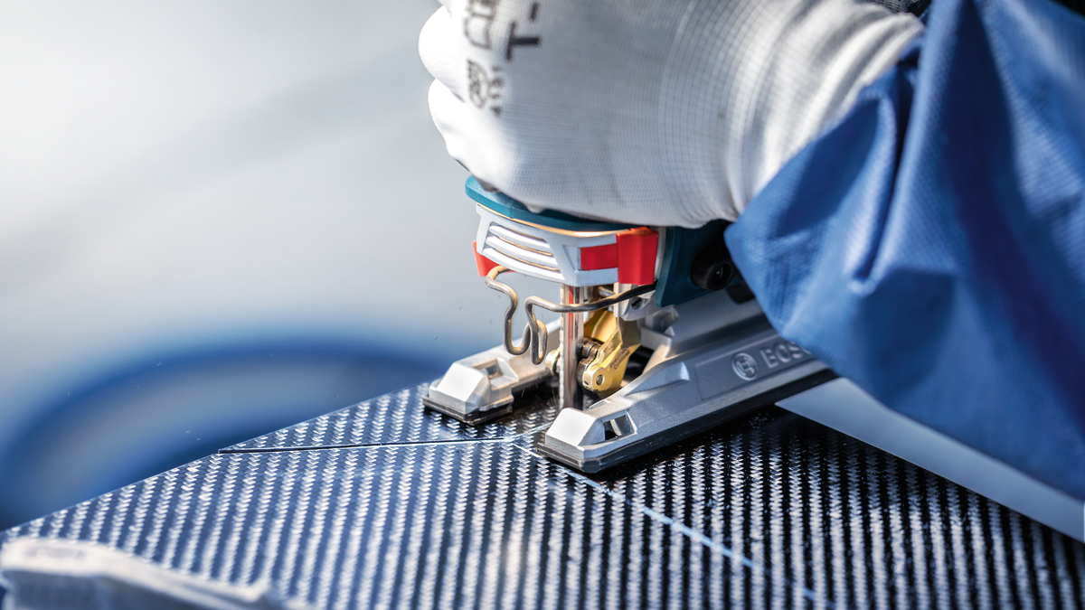 บุคคลที่สวมอุปกรณ์ความปลอดภัยกำลังตัดแผงที่มีลวดลายด้วยจิ๊กซอว์.