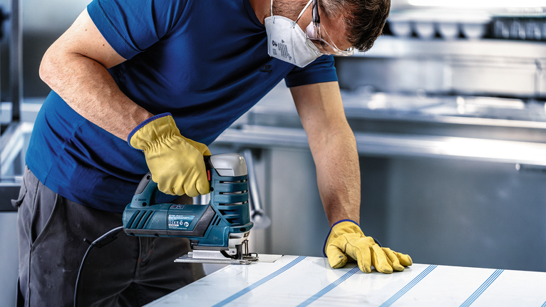 ผู้ที่สวมอุปกรณ์ความปลอดภัยใช้จิ๊กซอว์ตัดแผ่นโลหะ.