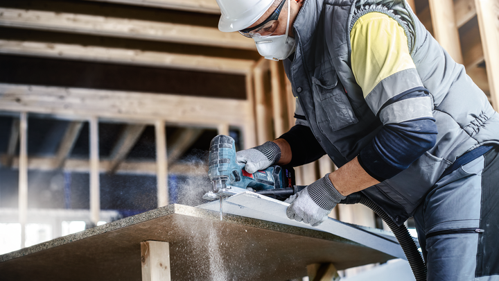 บุคคลที่สวมอุปกรณ์ความปลอดภัยตัดกระดานด้วยเครื่องมือไฟฟ้าในพื้นที่ก่อสร้าง.