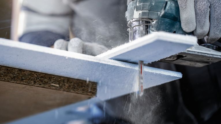 บุคคลที่สวมอุปกรณ์ความปลอดภัยกำลังตัดแผ่นฉนวนโฟมโดยใช้จิ๊กซอว์ไฟฟ้า.