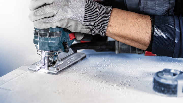 บุคคลที่สวมอุปกรณ์ความปลอดภัยใช้จิ๊กซอว์ตัดแผ่นวัสดุ.