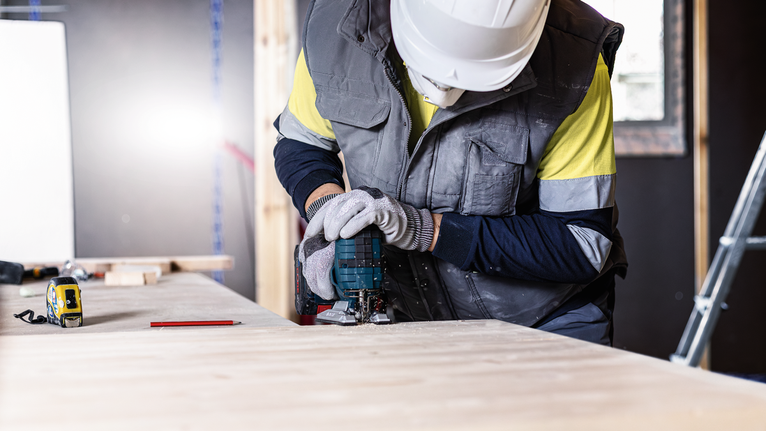 บุคคลที่สวมอุปกรณ์ความปลอดภัยใช้เครื่องมือไฟฟ้าตัดไม้บนโต๊ะทำงาน.