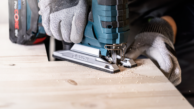 บุคคลที่สวมอุปกรณ์ความปลอดภัยใช้จิ๊กซอว์ไร้สายตัดแผ่นไม้.