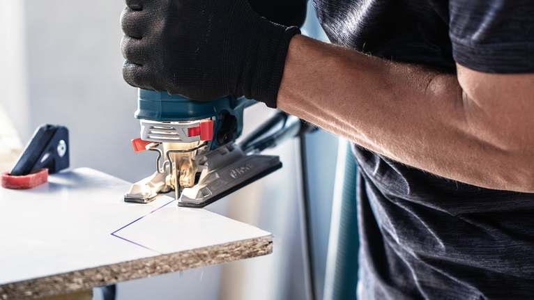 บุคคลที่สวมอุปกรณ์ความปลอดภัยกำลังตัดกระดานที่ทำเครื่องหมายไว้ด้วยจิ๊กซอว์.