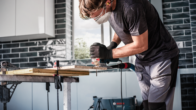 บุคคลที่สวมอุปกรณ์ความปลอดภัยใช้จิ๊กซอว์ตัดไม้บนโต๊ะทำงาน.