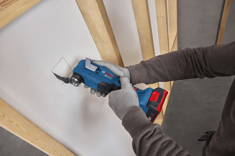 บุคคลที่สวมอุปกรณ์ด้านความปลอดภัยกำลังตัดช่องสี่เหลี่ยมในผนัง drywall โดยใช้เครื่องมืออเนกประสงค์