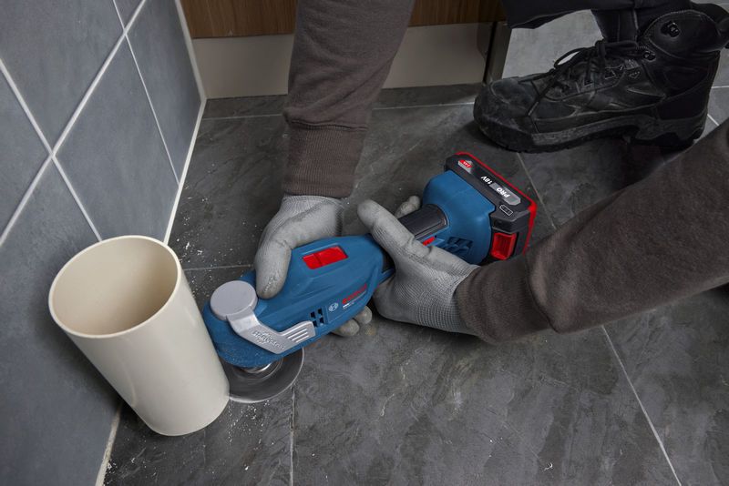 ผู้ที่สวมอุปกรณ์ความปลอดภัยใช้เครื่องมืออเนกประสงค์ตัดกระเบื้องพื้นข้างท่อ