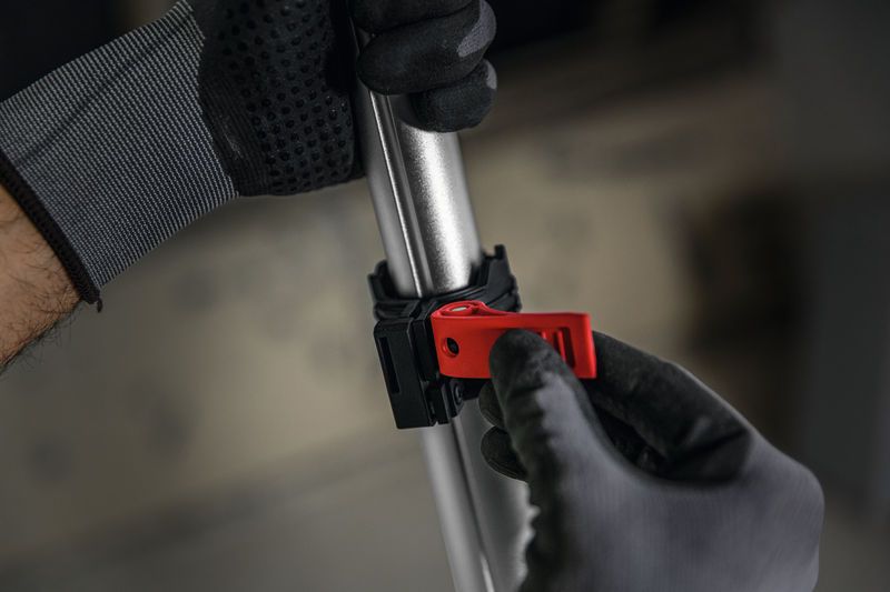 บุคคลที่สวมอุปกรณ์ด้านความปลอดภัยกำลังปรับที่หนีบสีแดงบนเสาโลหะ