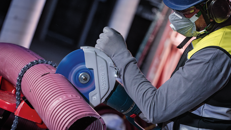 ผู้ที่สวมอุปกรณ์ความปลอดภัยกำลังตัดท่อพลาสติกขนาดใหญ่ด้วยเครื่องตัดไฟฟ้า