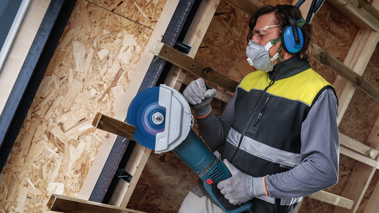 บุคคลที่สวมอุปกรณ์ความปลอดภัยกำลังตัดไม้ด้วยเลื่อยวงเดือนขนาดใหญ่