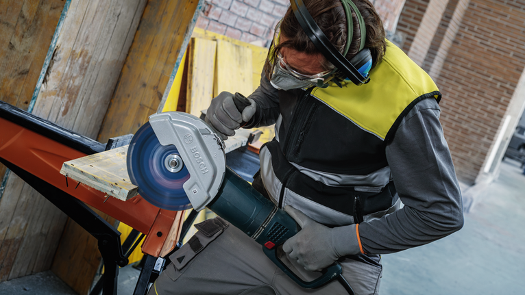 บุคคลที่สวมอุปกรณ์ความปลอดภัยกำลังตัดไม้กระดานด้วยเลื่อยวงเดือนขนาดใหญ่