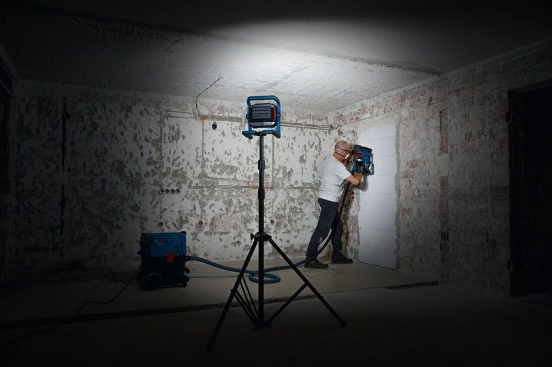 บุคคลที่สวมอุปกรณ์ความปลอดภัยกำลังใช้งานเครื่องเจาะผนังภายใต้แสงไฟทำงาน