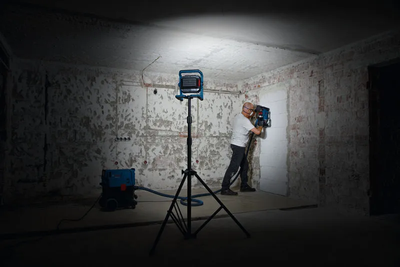 บุคคลที่สวมอุปกรณ์ความปลอดภัยกำลังใช้งานเครื่องเจาะผนังภายใต้แสงไฟทำงาน