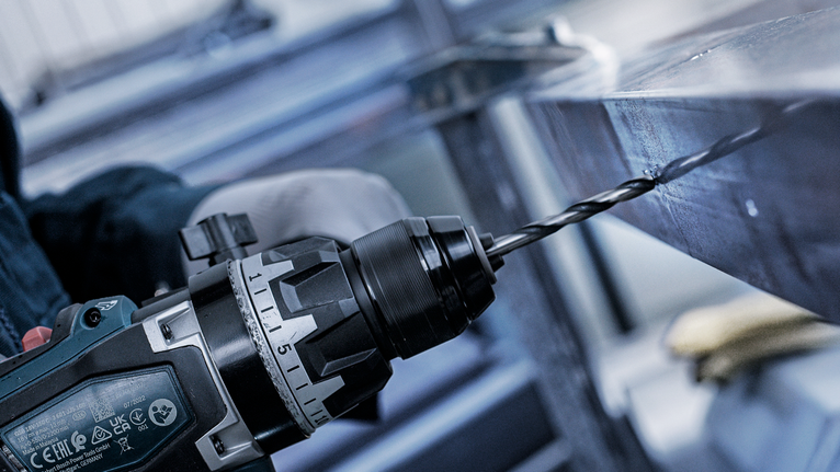 บุคคลที่สวมอุปกรณ์ความปลอดภัยกำลังเจาะรูบนคานโลหะ